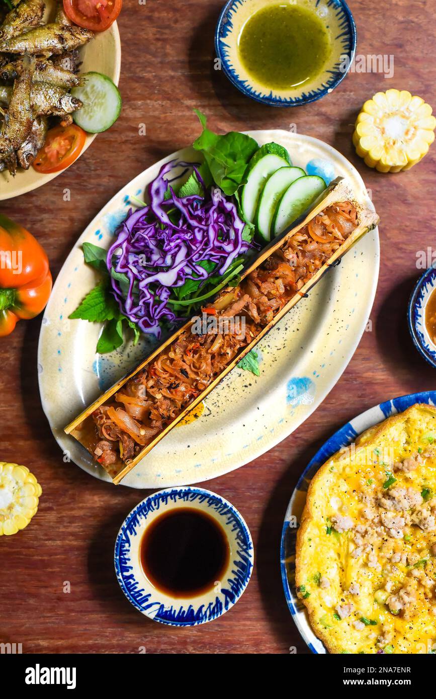 Conjunto de cocina vietnamita hecho de ciervo estofado en bambú, pescado frito, tortilla con salsas en mesa de madera Foto de stock