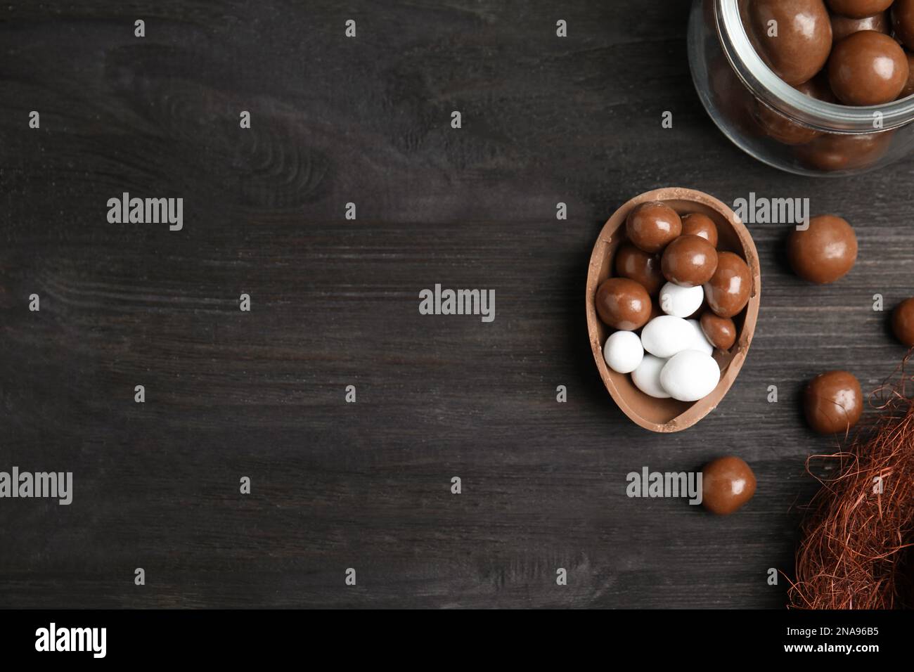 La mitad de sabroso huevo de chocolate y dulces en la mesa de madera negra, plana. Espacio para texto Foto de stock