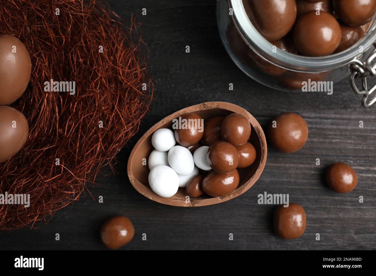 La mitad de sabroso huevo de chocolate, nido decorativo y dulces en la mesa de madera negra, tendido plano Foto de stock