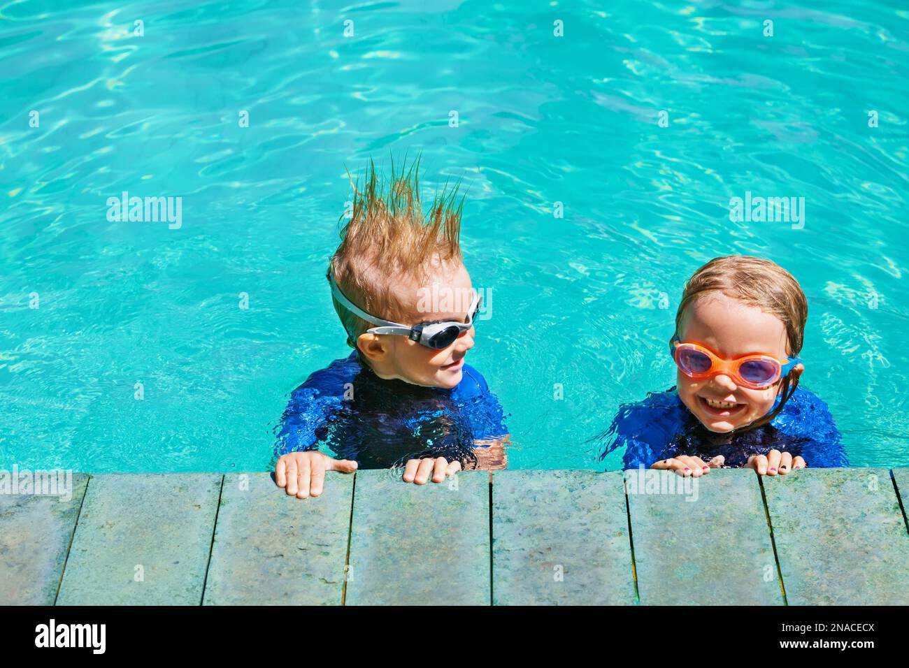 Los niños felices en trajes de neopreno y gafas aprenden a nadar, se  divierten junto a la piscina en el estilo de vida familiar saludable,  actividades deportivas acuáticas para niños pequeños Fotografía