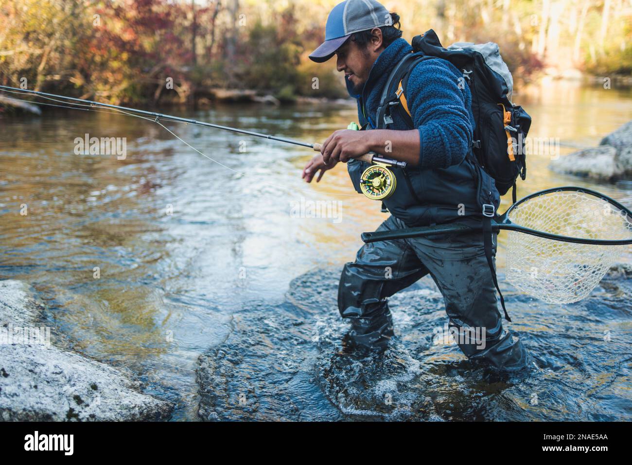 Un pescador de mosca vadeando a través de un arroyo a finales de temporada Foto de stock