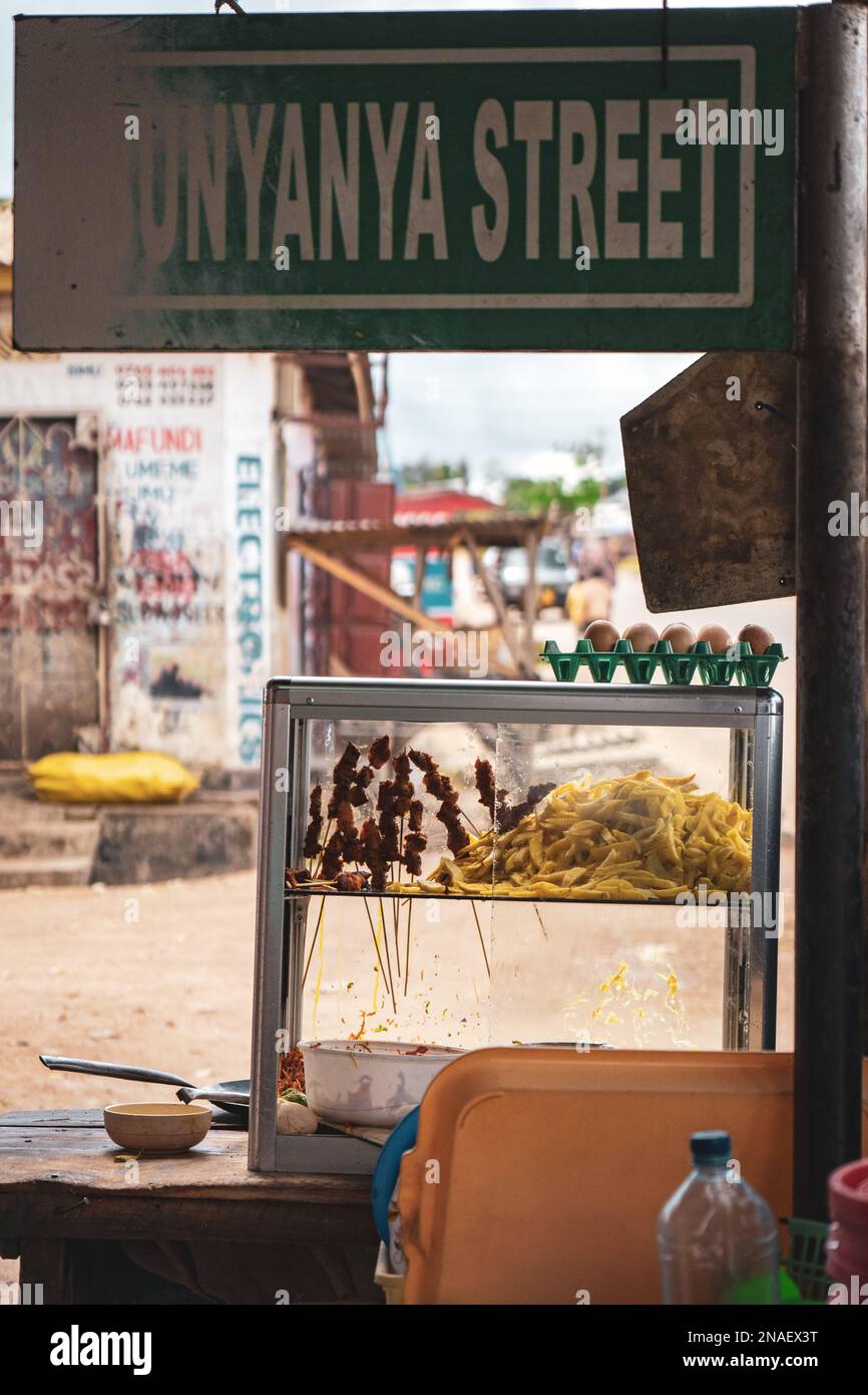 Puesto de comida rápida africana local. Señales de calles desgastadas. Patatas fritas, huevos, ensalada y carne almacenados en una caja de vidrio. Foto de stock