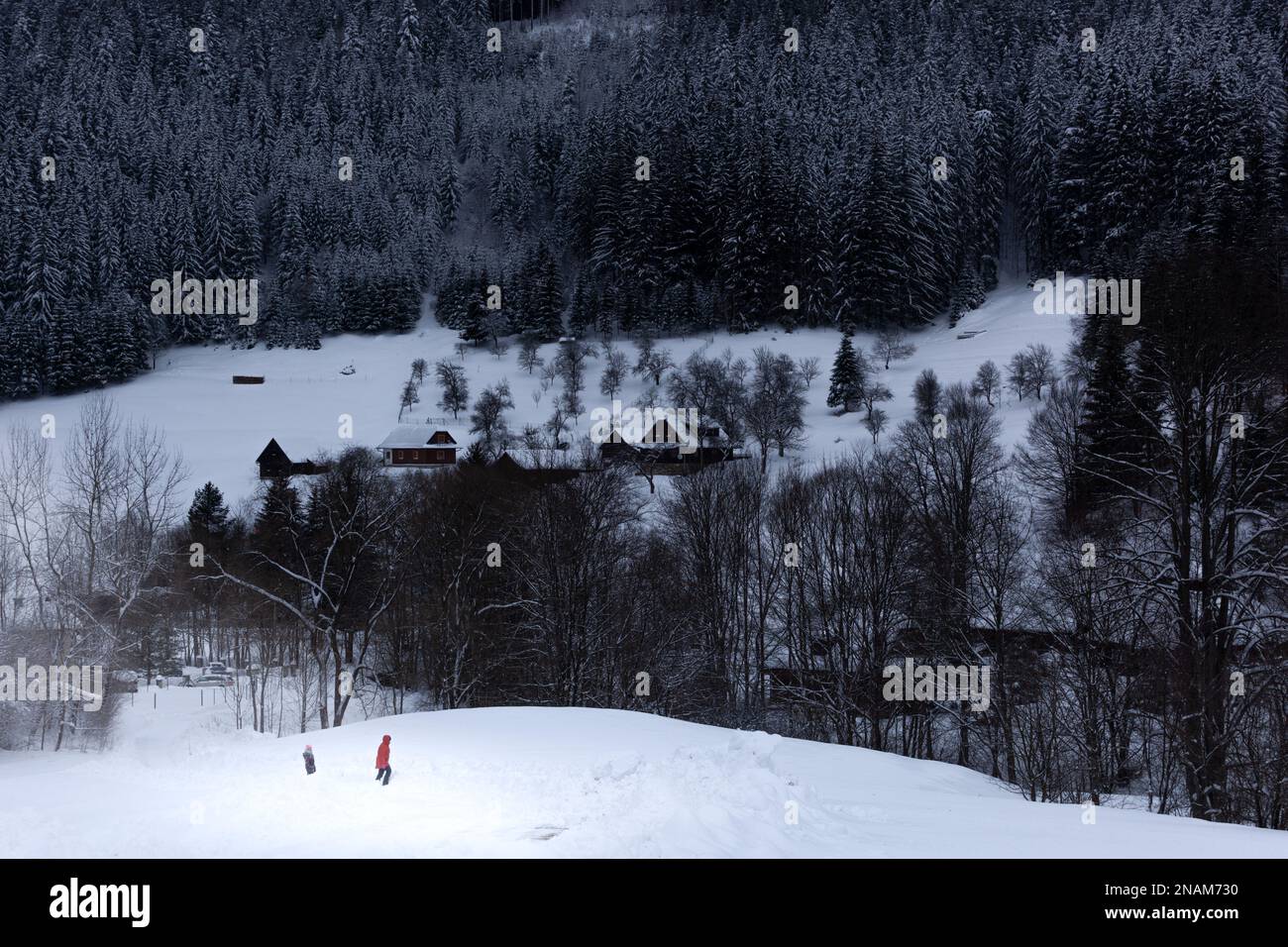 Dos personas están jugando en la nieve en primer plano. En la montaña en el fondo las casas tradicionales están dispuestas en el prado cubierto de sno Foto de stock