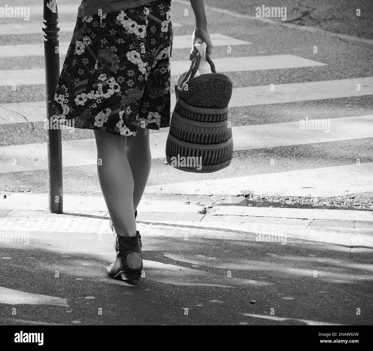 Mujer vistiendo falda floral y con cesta de la compra en mano cruzando calle parisina. París, Francia. Estado de ánimo primaveral en el aire. Foto blanco negro Foto de stock
