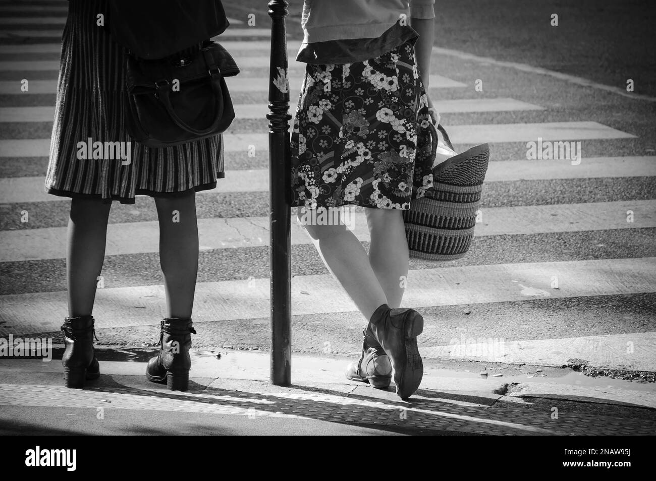 Dos mujeres con faldas esperando cruzar la calle parisina. Amigas pasan tiempo juntas. París, Francia. Estado de ánimo primaveral en el aire. Foto blanco negro Foto de stock
