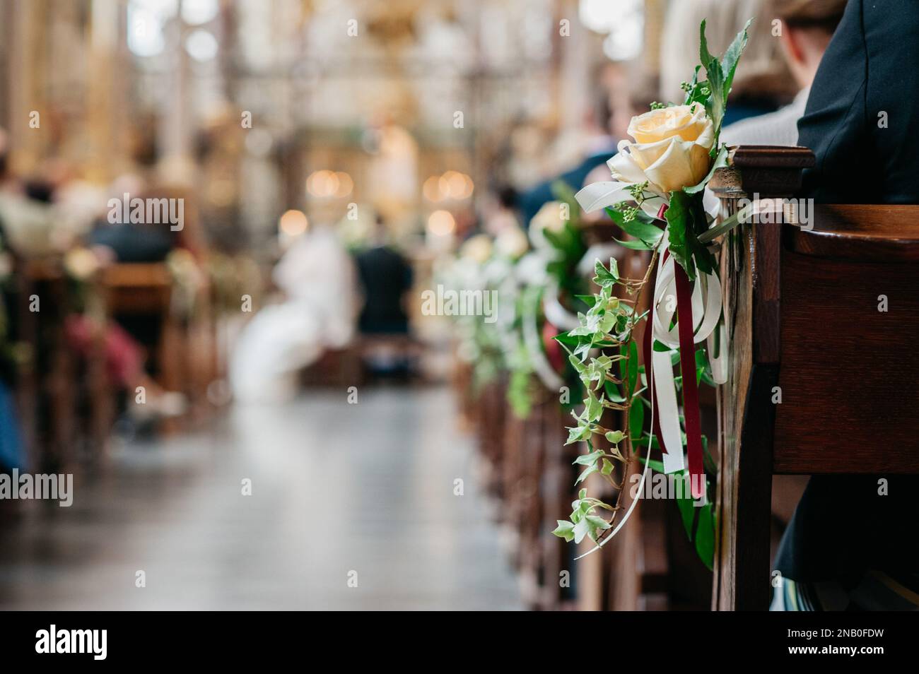 Las flores colgando en los escritorios de la iglesia mientras la gente está sentada en un evento de boda Foto de stock
