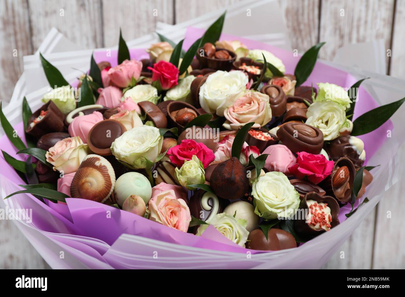 Hermoso ramo de flores y dulces de chocolate sobre fondo de madera blanca,  primer plano Fotografía de stock - Alamy