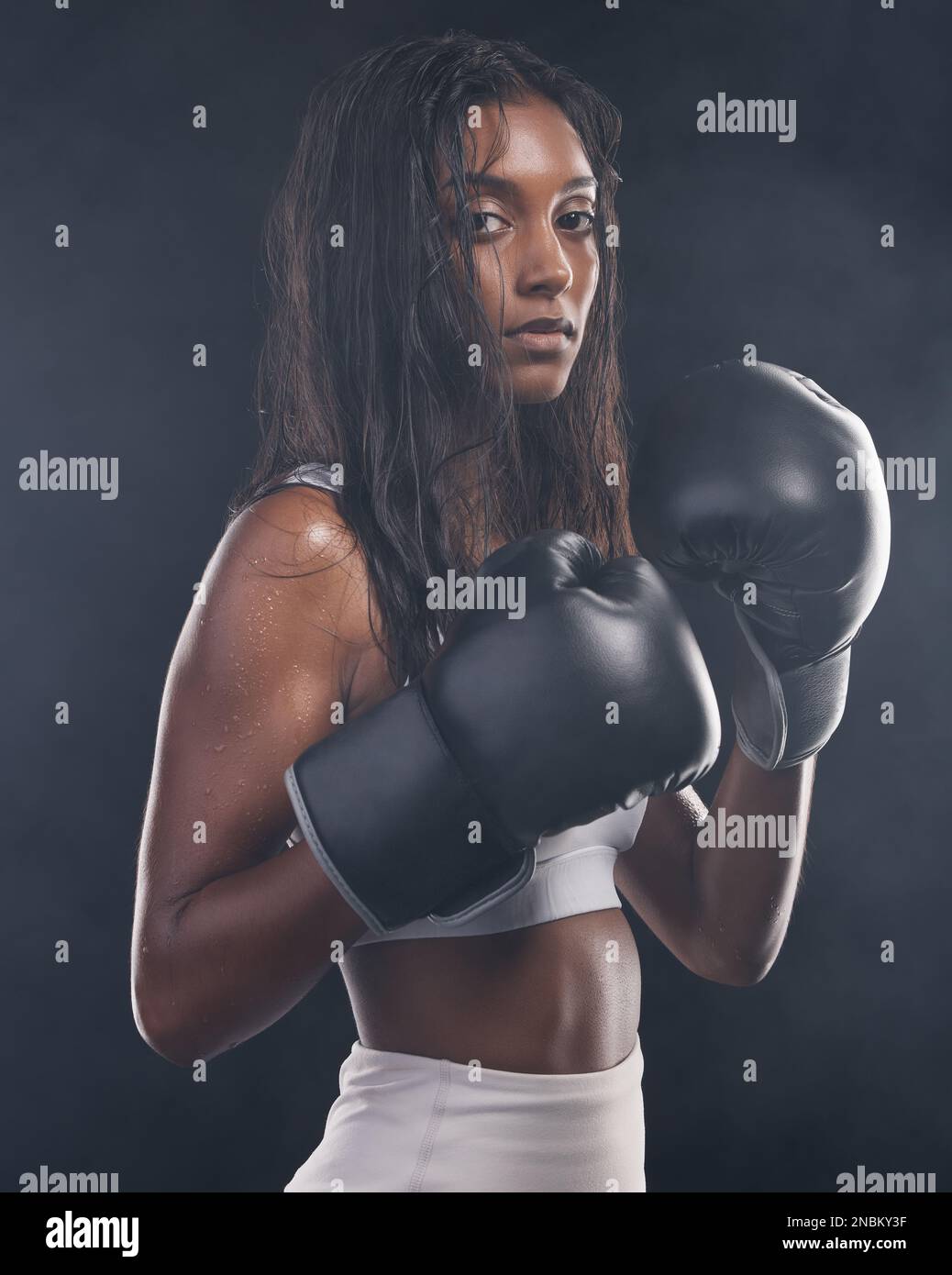 Guantes de boxeador, mujer y retrato sobre fondo negro para deportes, enfoque fuerte o entrenamiento mma. Boxeo femenino, campeón y puño pelea en estudio Foto de stock