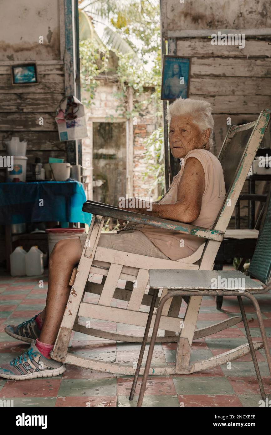 Augusto César Sandino, Artemisa, Cuba. 12th de julio de 2019. Mujer anciana sentada en un sillón de madera en una casa en una ciudad rural en Cuba. Foto de stock