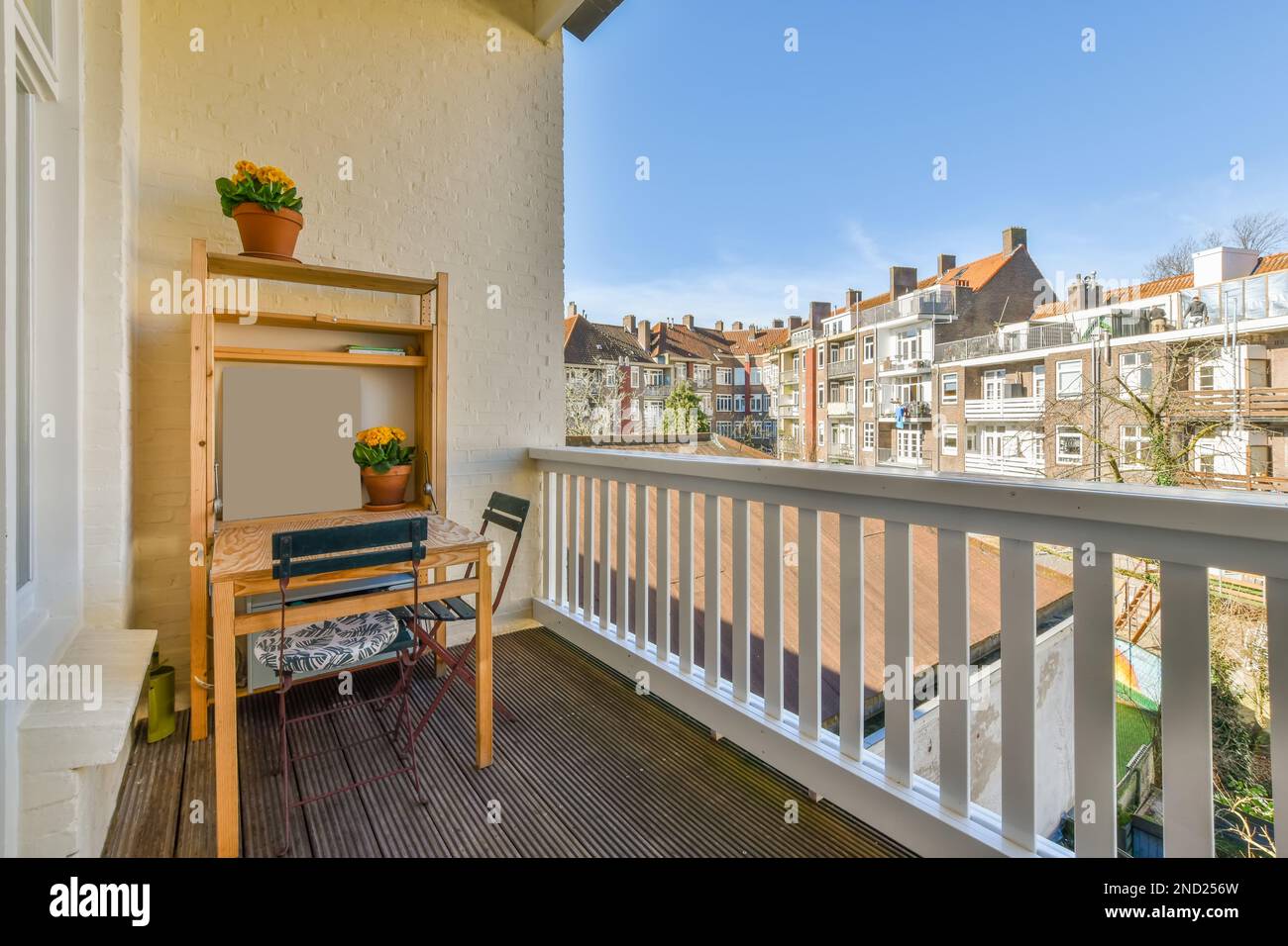 Balcón con valla blanca y escritorio de madera cerca de plantas en macetas  y sillas en piso moderno contra el paisaje urbano Fotografía de stock -  Alamy