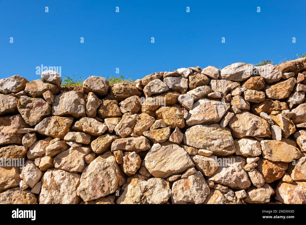 pared de piedra suelta apilada contra un fondo de cielo azul Foto de stock