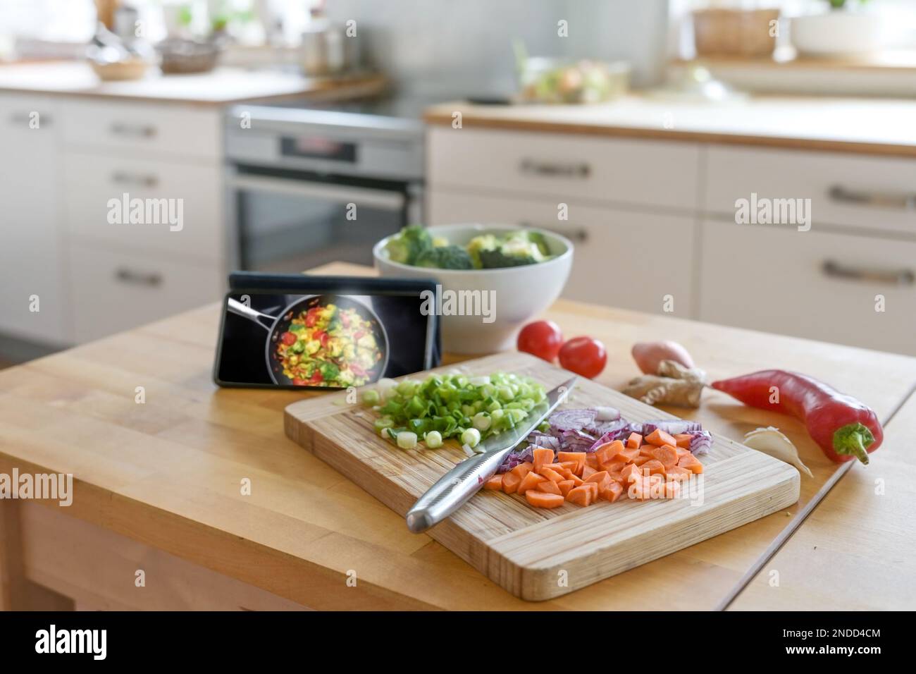 Cocinar mediante el uso de una aplicación en línea. Smartphone, verduras en dados y un cuchillo en una tabla de madera, cocina borrosa en el fondo, enfoque seleccionado, estrecho Foto de stock