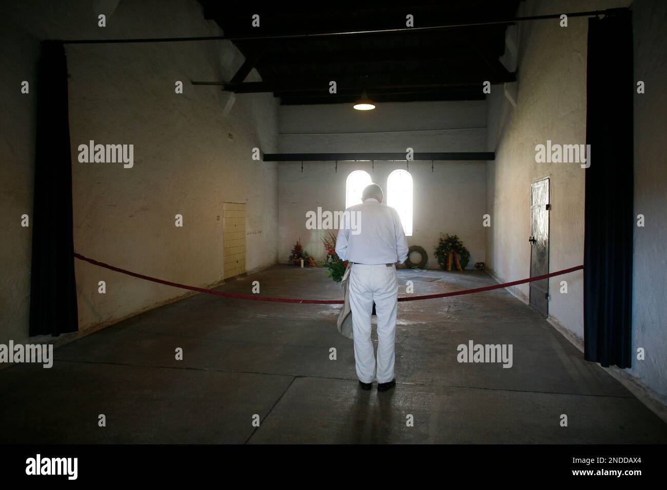 A man takes a minute of silence in front of a steel girder with hooks in the former execution