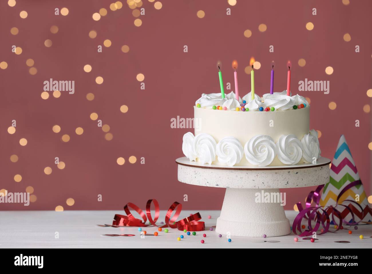 Pastel de cumpleaños con velas ardientes y decoración en mesa blanca contra  luces festivas borrosas, espacio para texto Fotografía de stock - Alamy