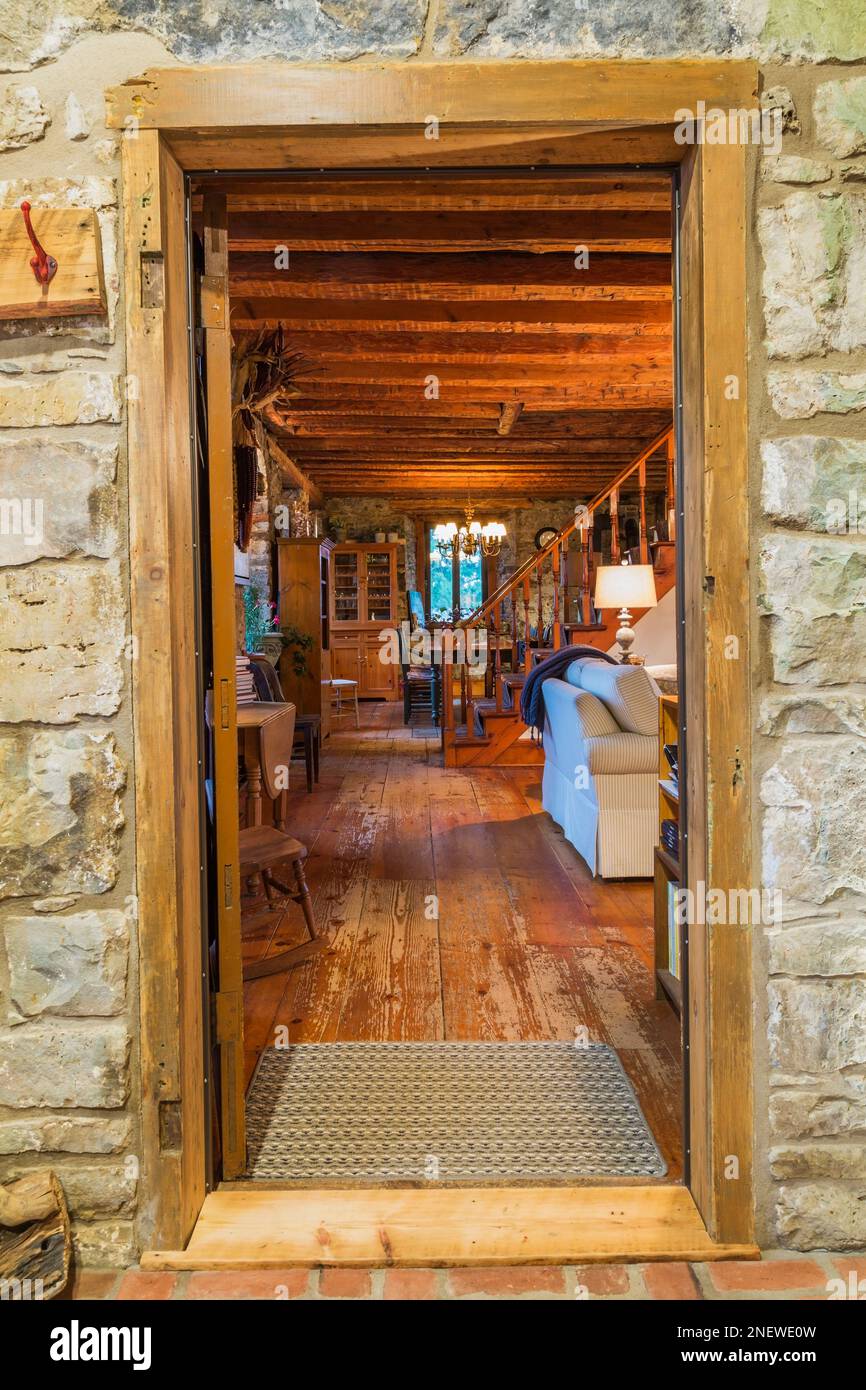 Puerta alrededor de la pared de piedra de campo en extensión que muestra la sala de estar y las escaleras de madera de pino dentro de la antigua casa de piedra cortada estilo cabaña de 1820 y la casa de piedra de campo. Foto de stock