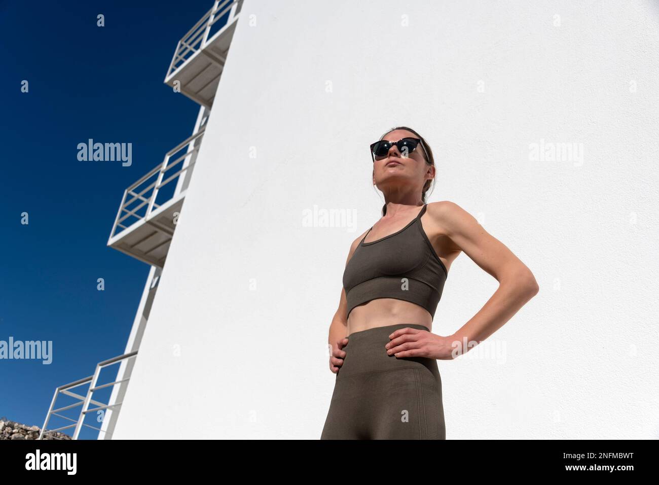 Retrato de primer plano de la mujer de mediana edad en ropa deportiva con gafas de sol, listo para hacer ejercicio al aire libre bajo el sol Foto de stock