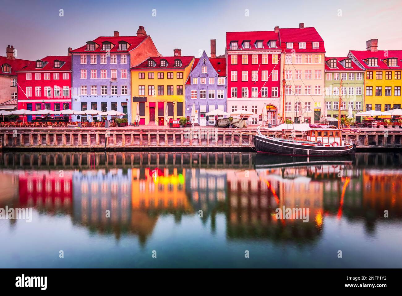 Copenhague, Dinamarca. Nyhavn, el icónico canal de Kobenhavn, refleja edificios coloridos y farolas brillantes en el crepúsculo, creando un pintoresco touris Foto de stock