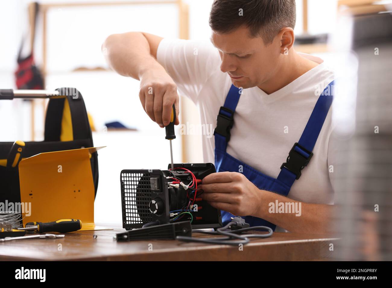 Técnico profesional que repara el calentador del ventilador eléctrico con  el destornillador en la mesa en el interior Fotografía de stock - Alamy