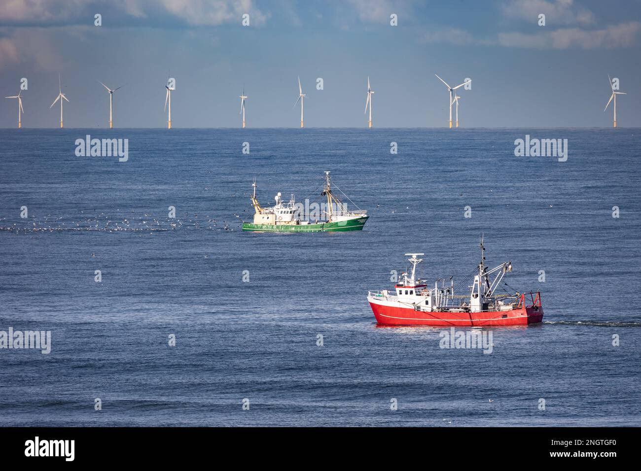 Dos cortadores pasándose en el Mar del Norte con turbinas eólicas de un parque eólico en el fondo Foto de stock