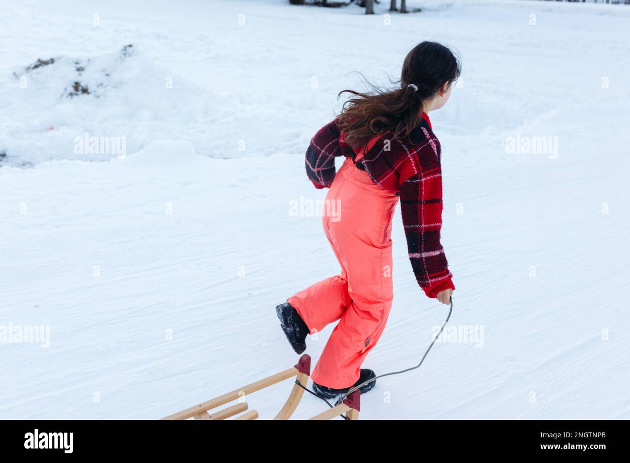 chica con el pelo largo oscuro en jersey rojo y pantalones de esquí naranja  huye con trineo de madera en carretera nevada Fotografía de stock - Alamy