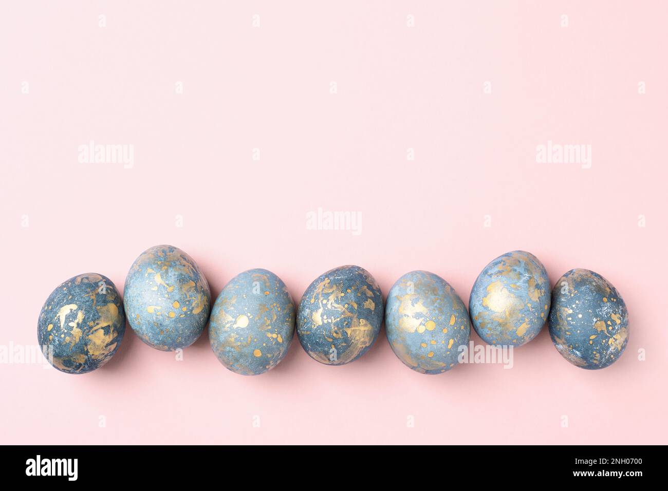 Huevos de Pascua azules y dorados en fila sobre fondo rosa pastel de Pascua, tarjeta de felicitación, espacio de copia, plano, Foto de stock