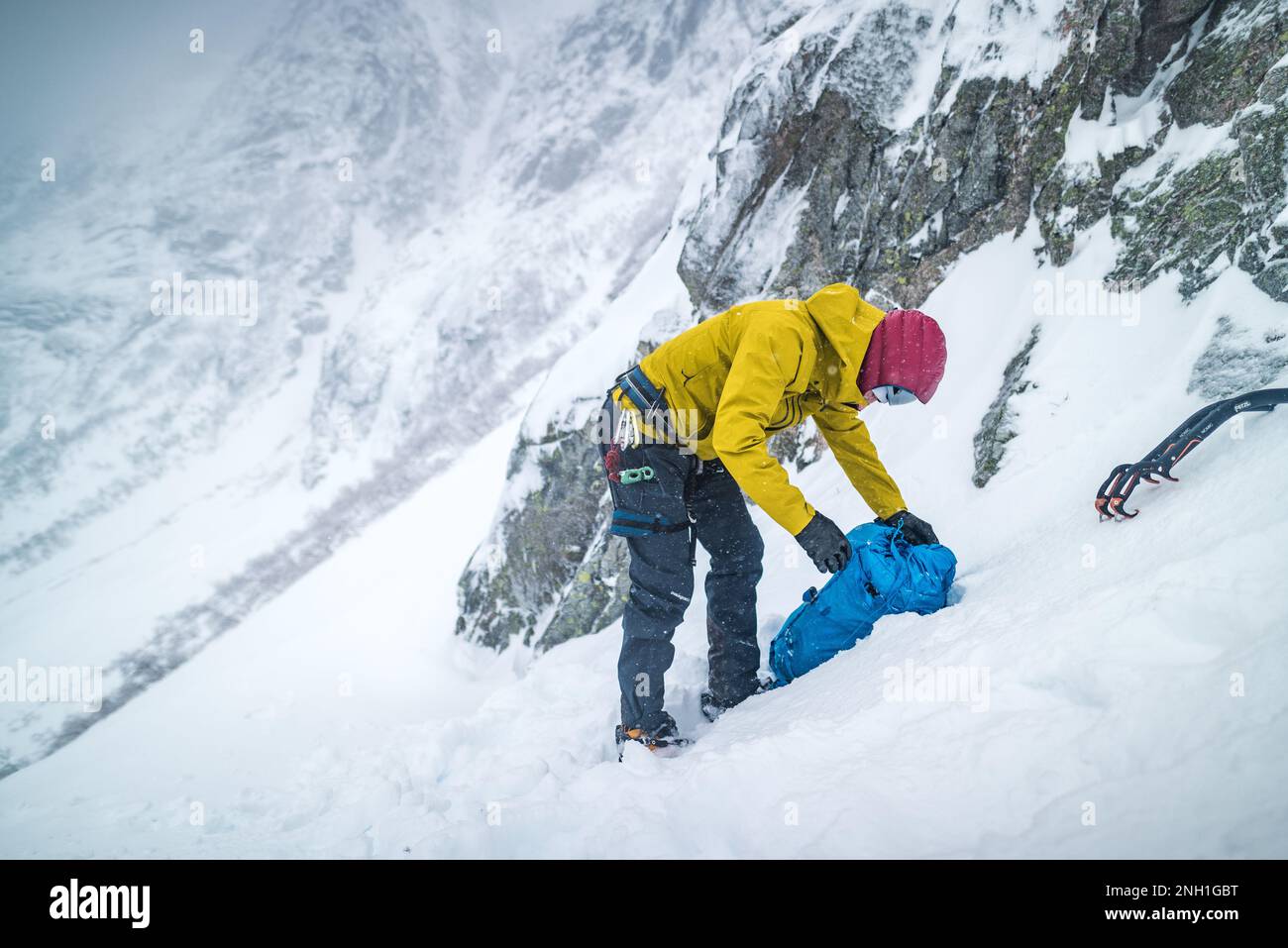 Hombre que se prepara para escalar el hielo rodeado de paisaje nevado Foto de stock