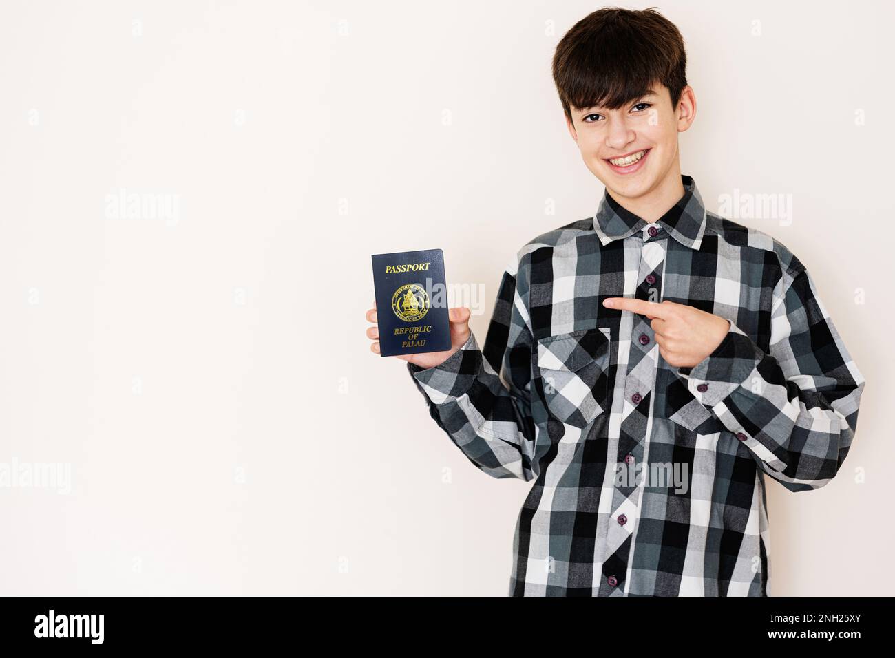 Muchacho adolescente joven que sostiene el pasaporte de Palau que se ve positivo y feliz de pie y sonriendo con una sonrisa confiada contra el fondo blanco. Foto de stock