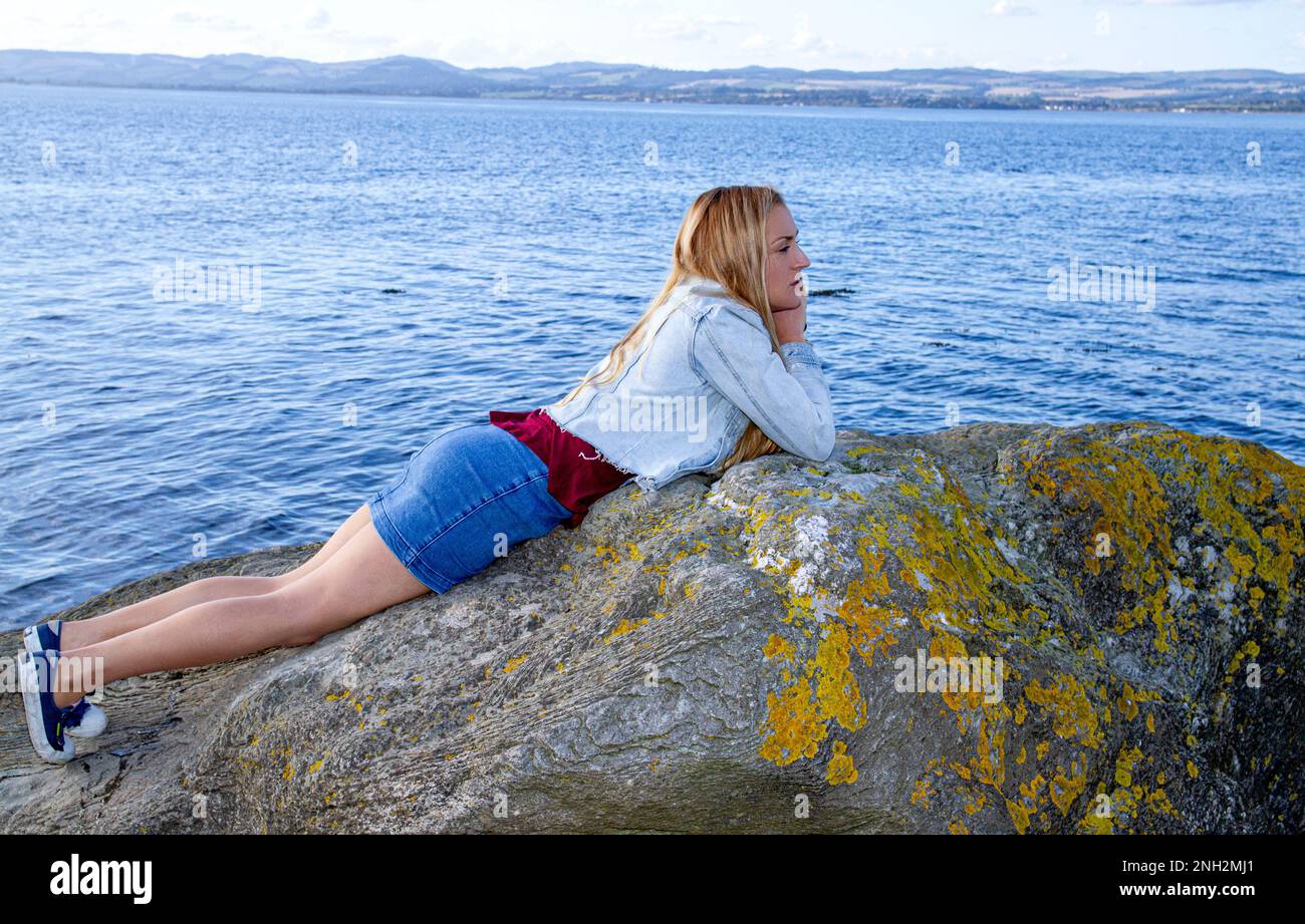 En un hermoso día de octubre en Wormit Beach, Fife, Rhianna Martin se encuentra en grandes rocas junto al río Tay, Escocia Foto de stock