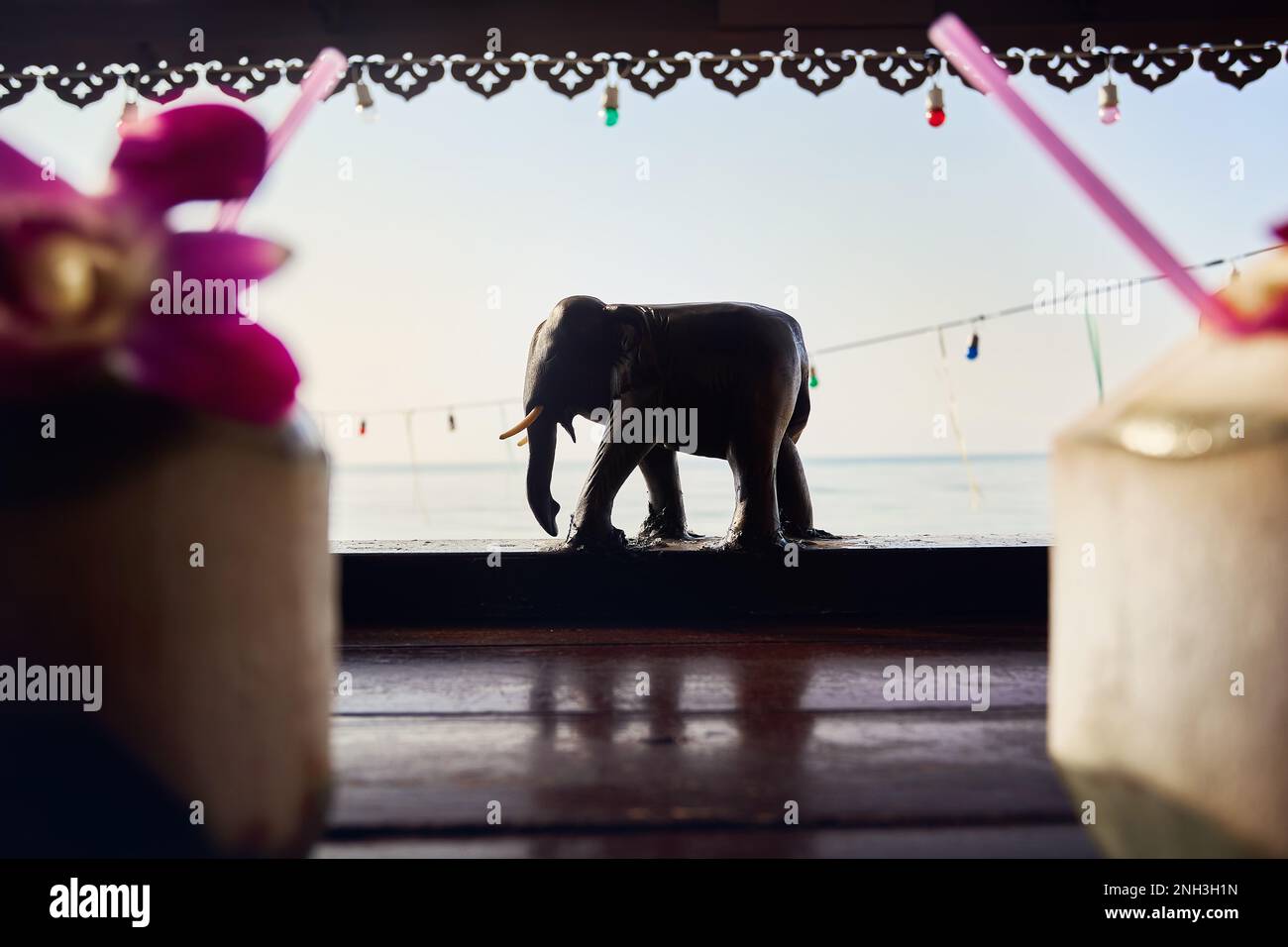 Decoración de la estatua de elefante de madera del complejo en la playa tropical al amanecer con dos cocoteros en primer plano sobre la mesa Foto de stock