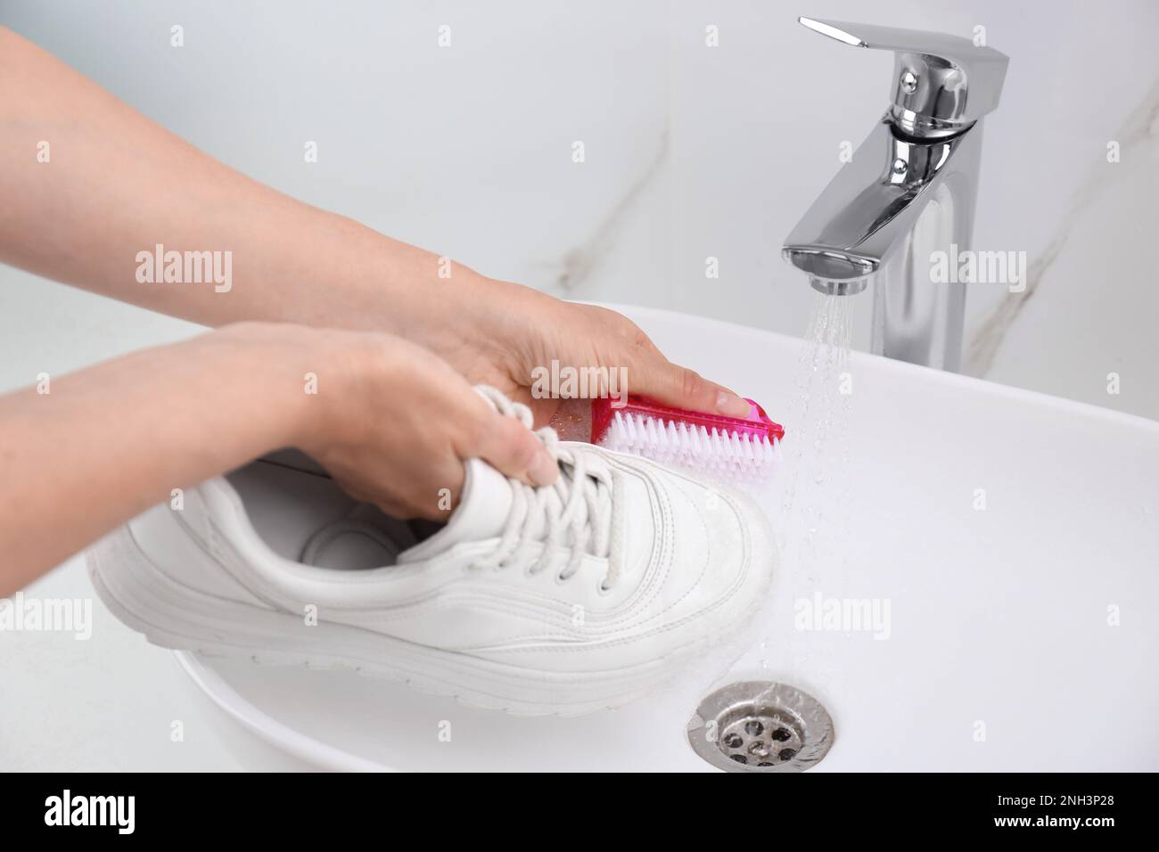 Mujer que lava el zapato con el cepillo debajo del agua del grifo en fregadero, closeup Foto de stock