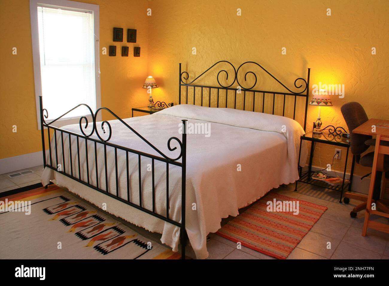 Dormitorio dorado en el Montebello Bed and Breakfast Inn con una cama de hierro forjado y alfombras mexicanas en el suelo. Foto de stock