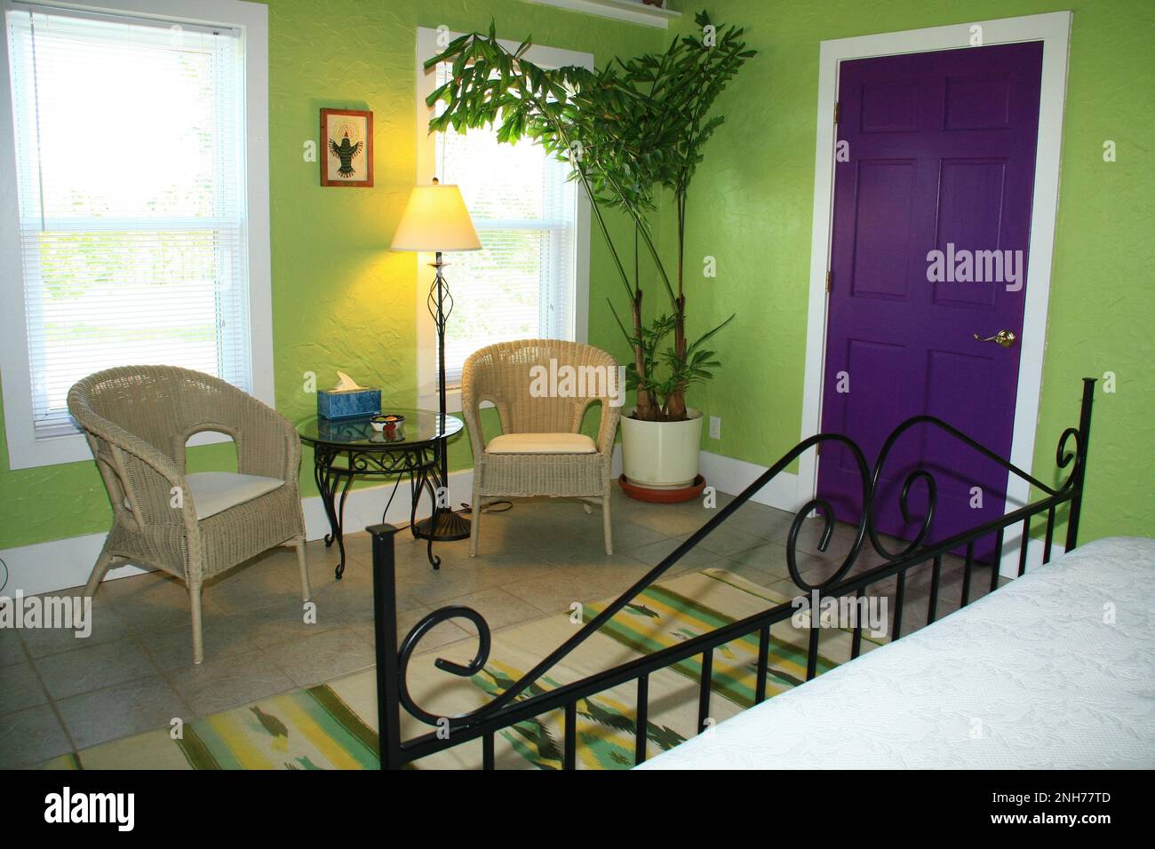 Sala de estar de un dormitorio verde con sillas de ratán, mesa, lámpara, puerta púrpura y final de cama de hierro forjado en Montebello Bed and Breakfast Inn Fotografía de