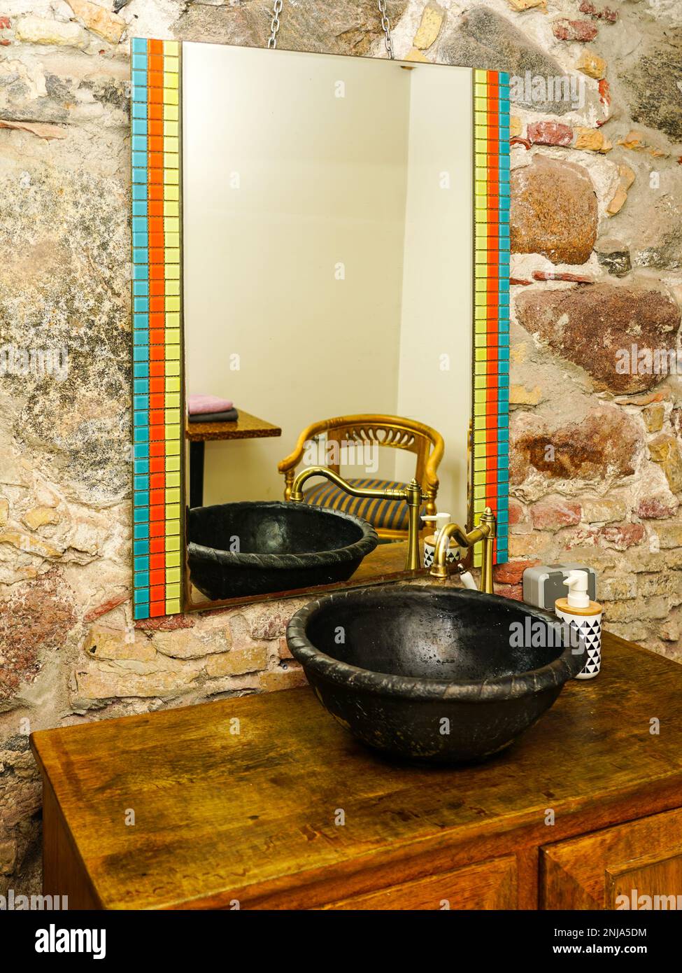 Interior de baño de estilo vintage con fregadero de cerámica redondo negro  con grifo de latón en la parte superior del gabinete de madera viejo, fondo  de pared de piedra Fotografía de