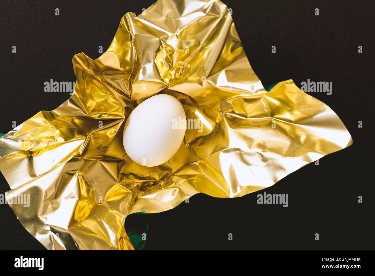 Un huevo blanco envuelto en papel dorado brillante metálico sobre fondo  negro Fotografía de stock - Alamy