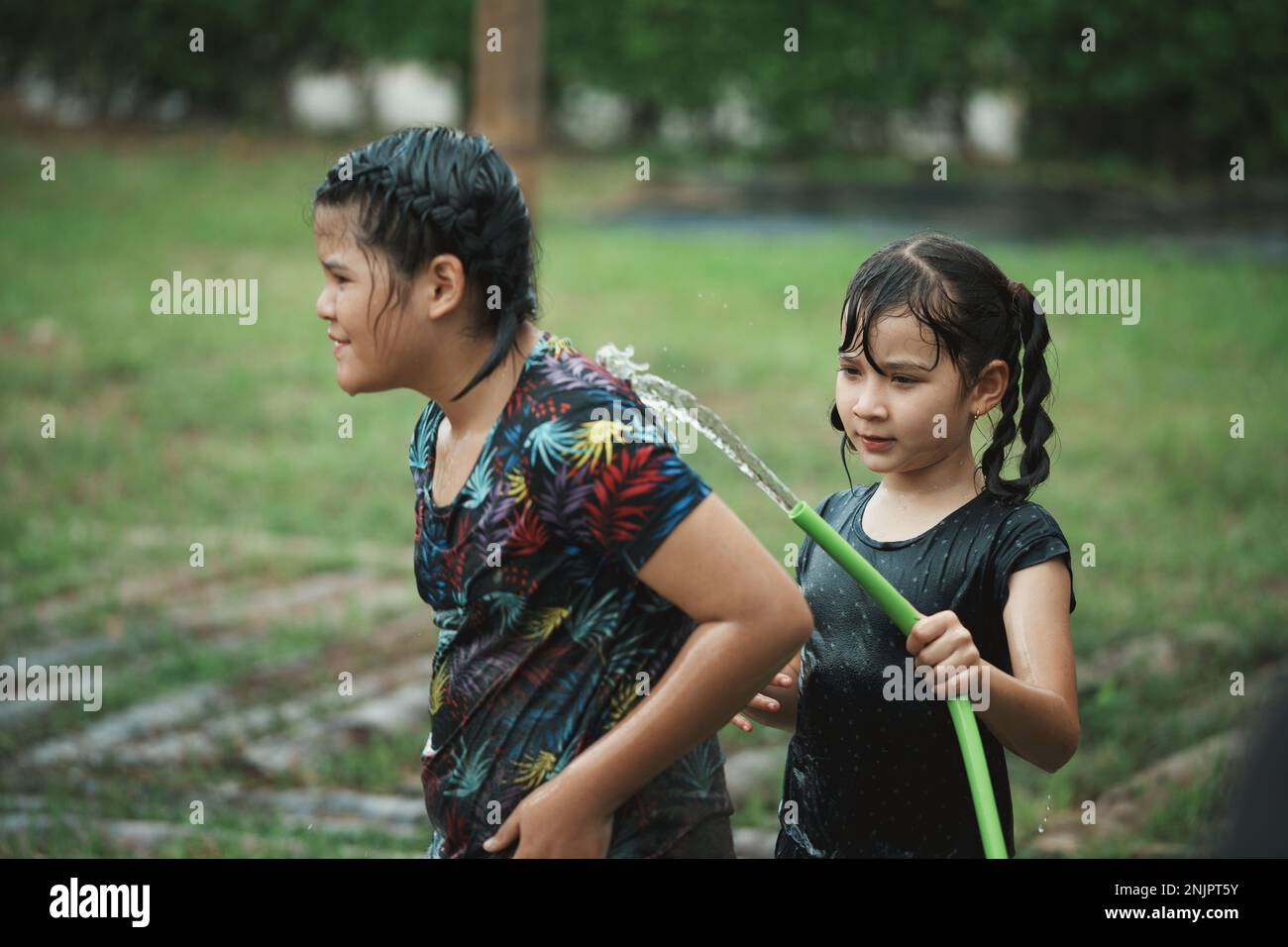 Dos niña niño se divierte jugando en el agua de la manguera al aire libre. Niña que limpia el barro sucio por el agua de la manguera exterior. Foto de stock