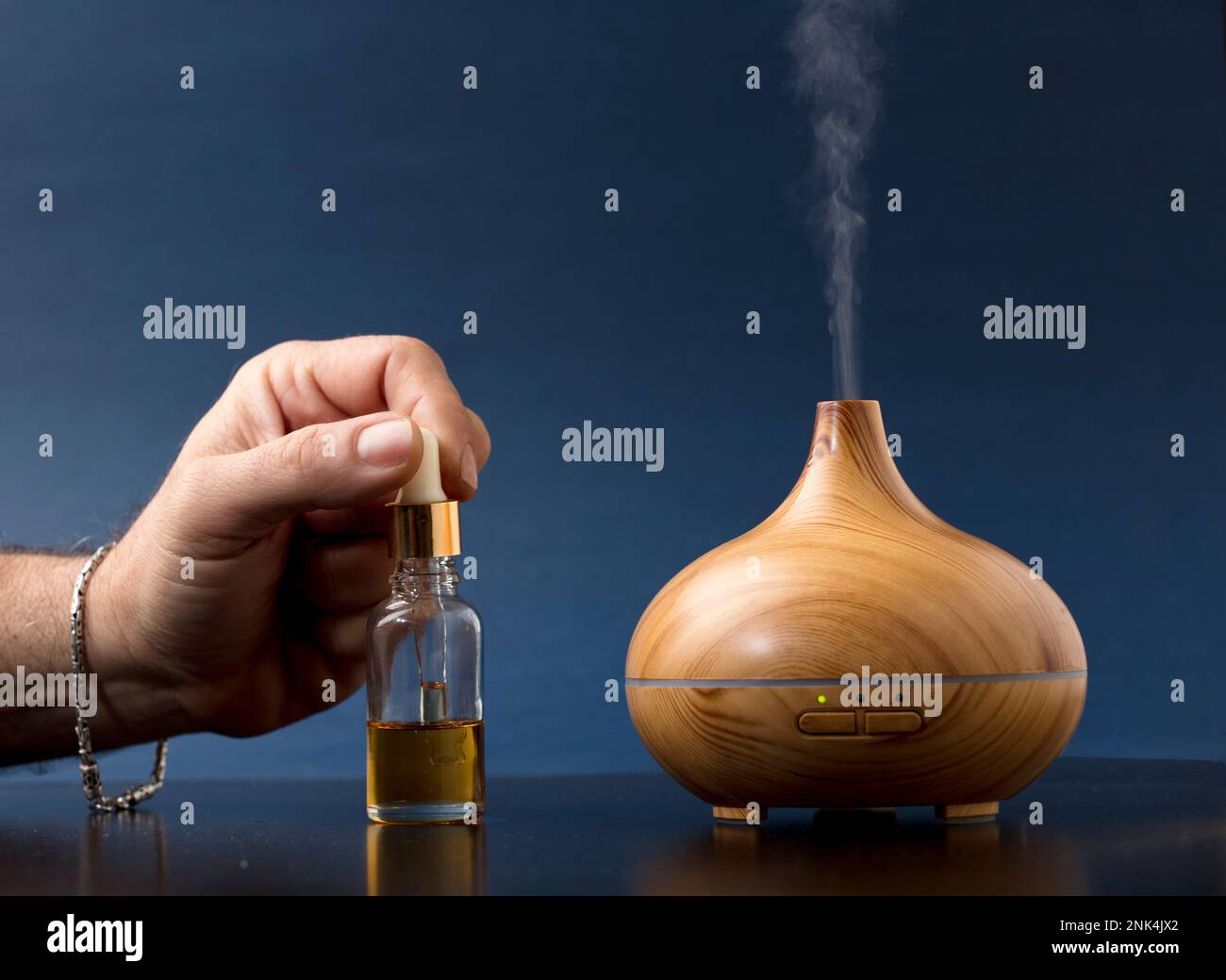 ambientador de madera con vapor de esencias naturales, mano del hombre con  pulsera recargándolo, fondo azul Fotografía de stock - Alamy