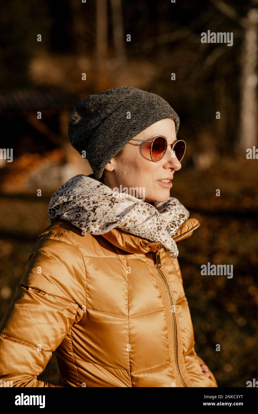 Mujer sonriente con gafas de sol y ropa de invierno de pie bajo la