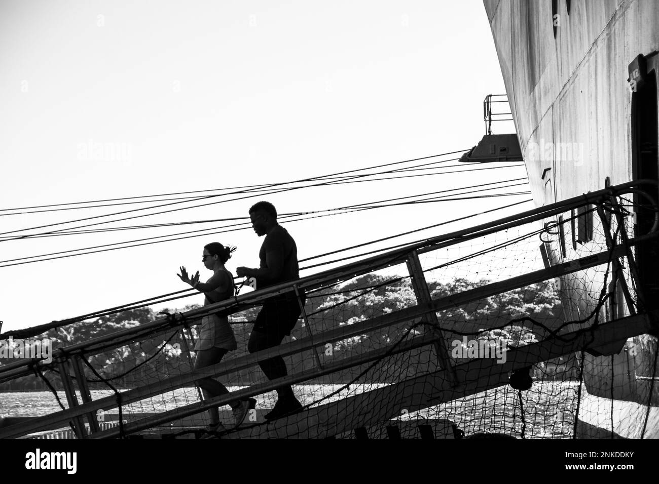 Una imagen en blanco y negro de alto contraste de dos personas caminando por la pasarela de un crucero, Roatán, Honduras. Foto de stock