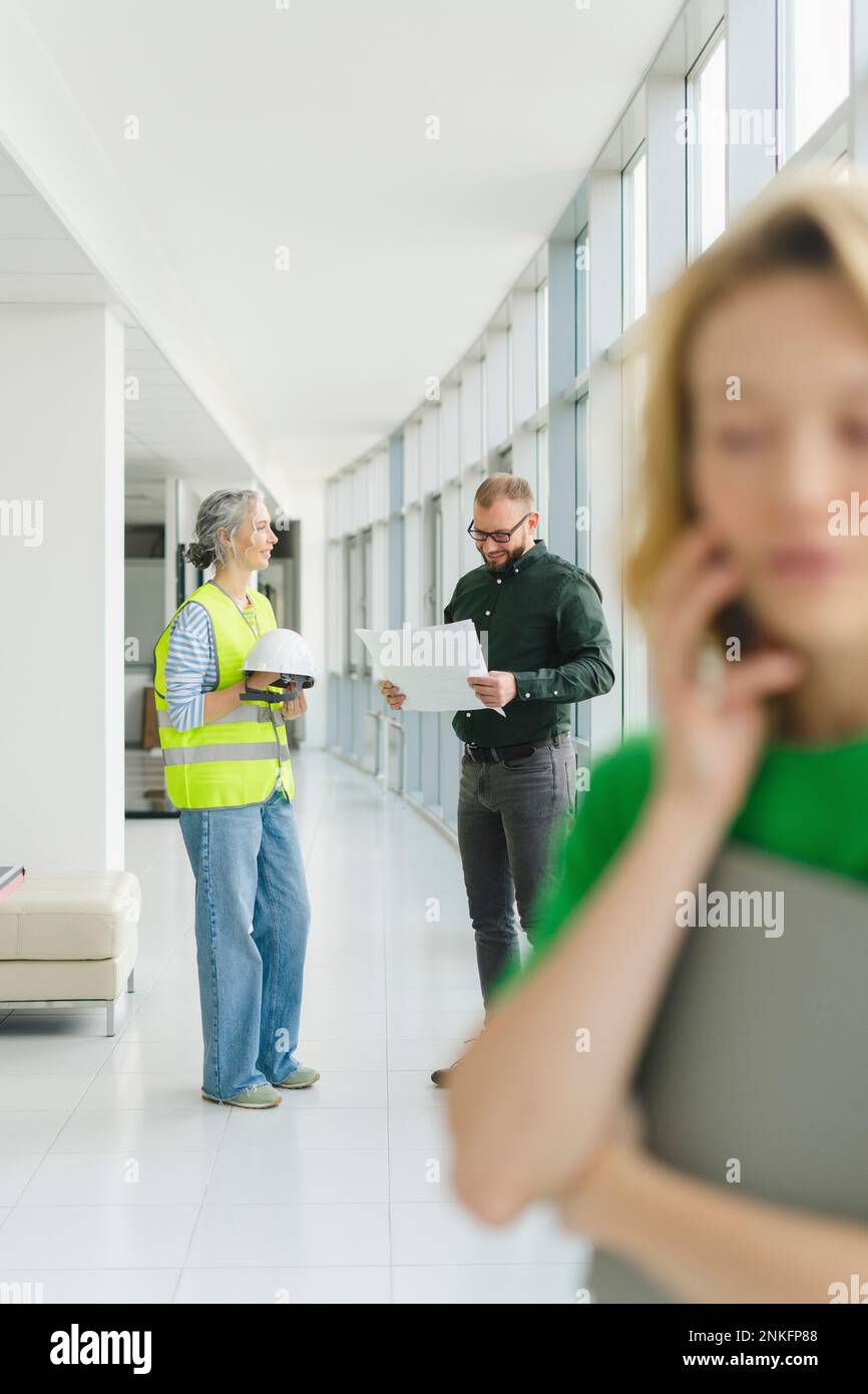 Reunión del hombre de negocios con el ingeniero en el piso de la oficina con la mujer en el teléfono en primer plano Foto de stock