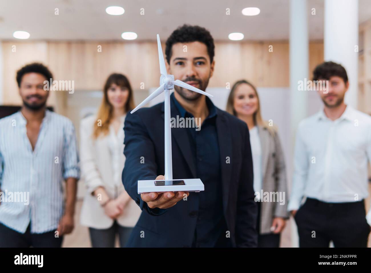 Hombre de negocios sosteniendo el modelo de turbina de viento delante de su equipo en la oficina Foto de stock