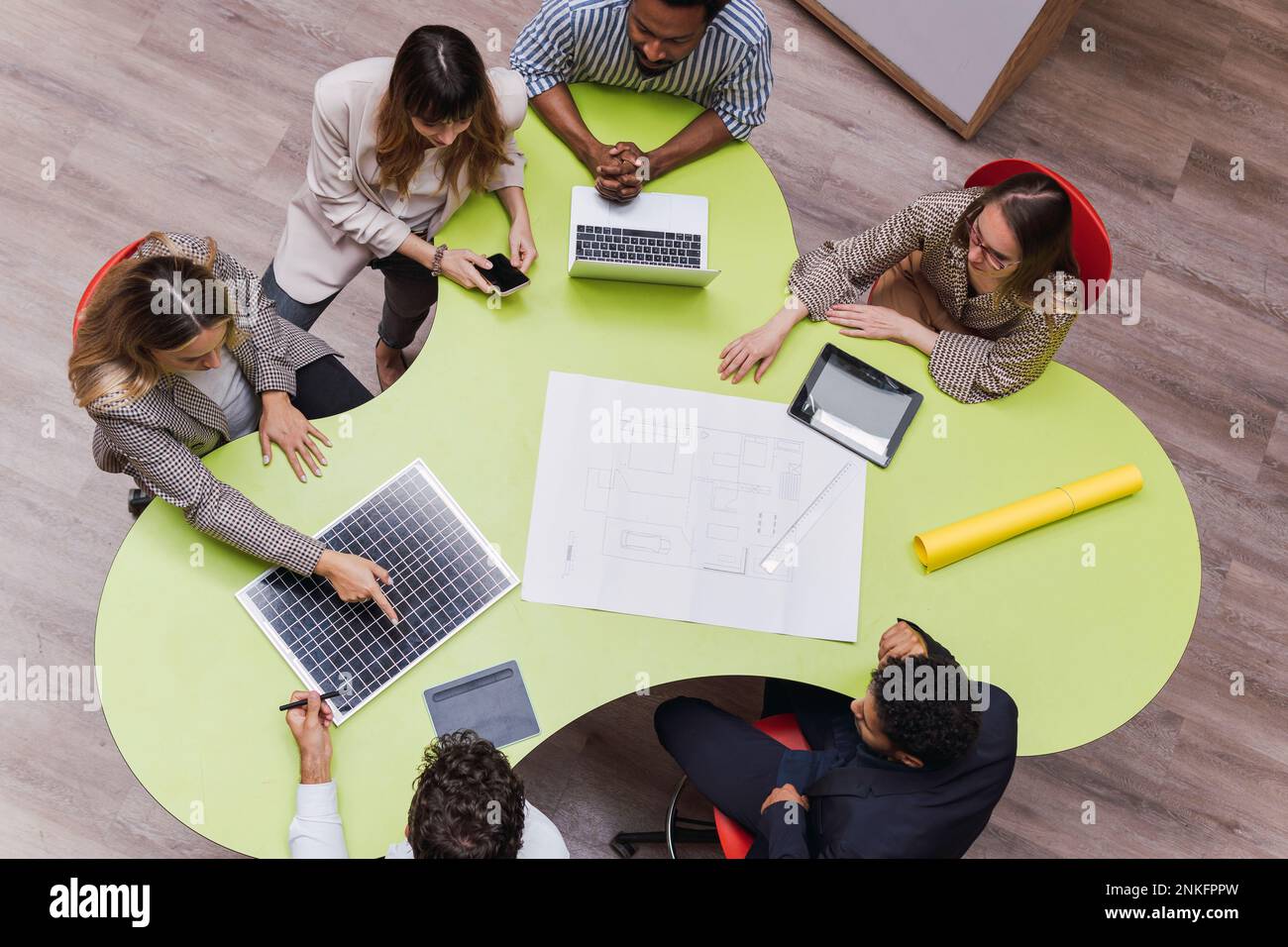 Vista de ángulo alto de los colegas de negocios que tienen una reunión con plan, dispositivos inalámbricos y panel solar en la mesa Foto de stock