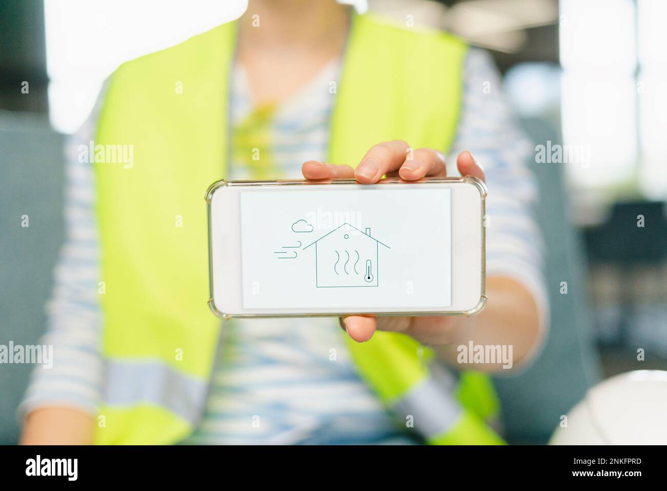 Mujer que lleva ropa reflexiva que sostiene el teléfono móvil con la casa en exhibición Foto de stock