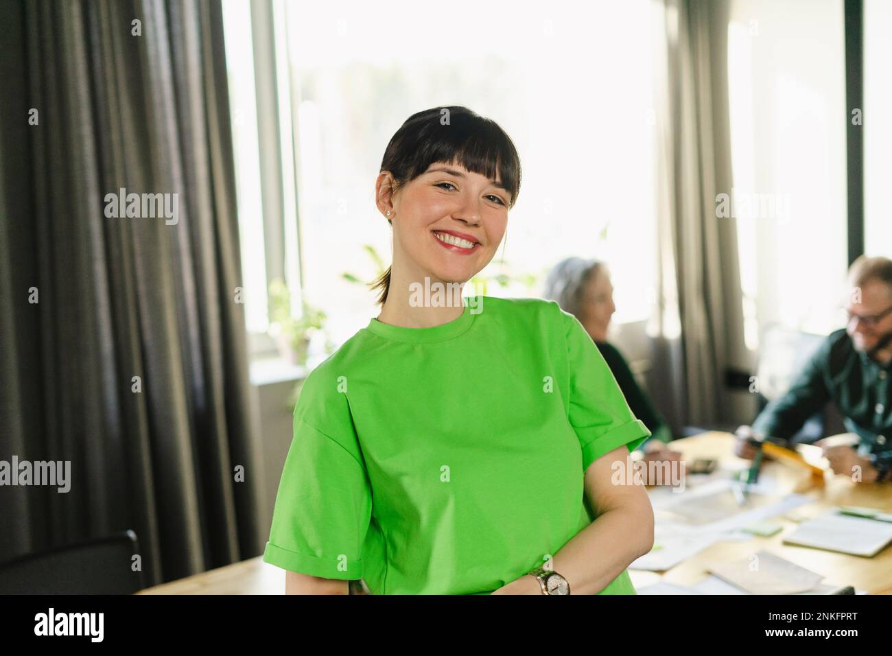 Retrato de mujer sonriente con camiseta verde durante una reunión en sala de conferencias Foto de stock