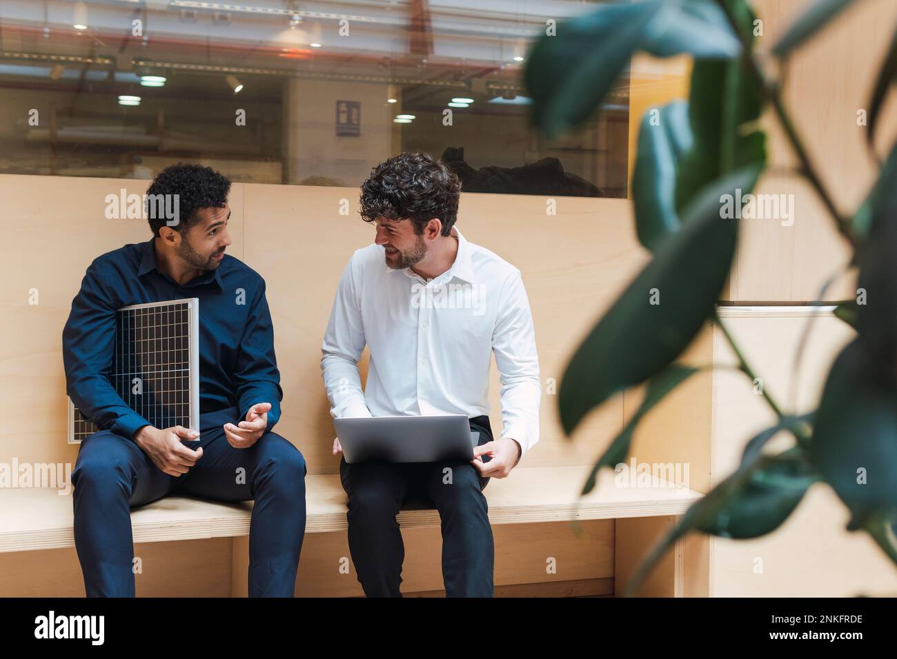 Hombre de negocios con el panel solar y colega con el ordenador portátil hablando en la oficina Foto de stock