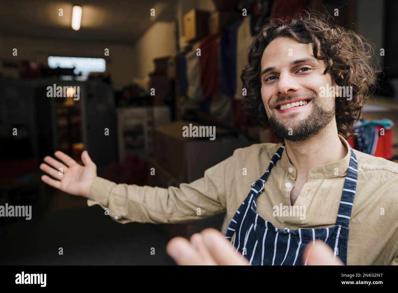 Hombre de negocios joven feliz que lleva delantal que invita en la sala de almacenamiento Foto de stock