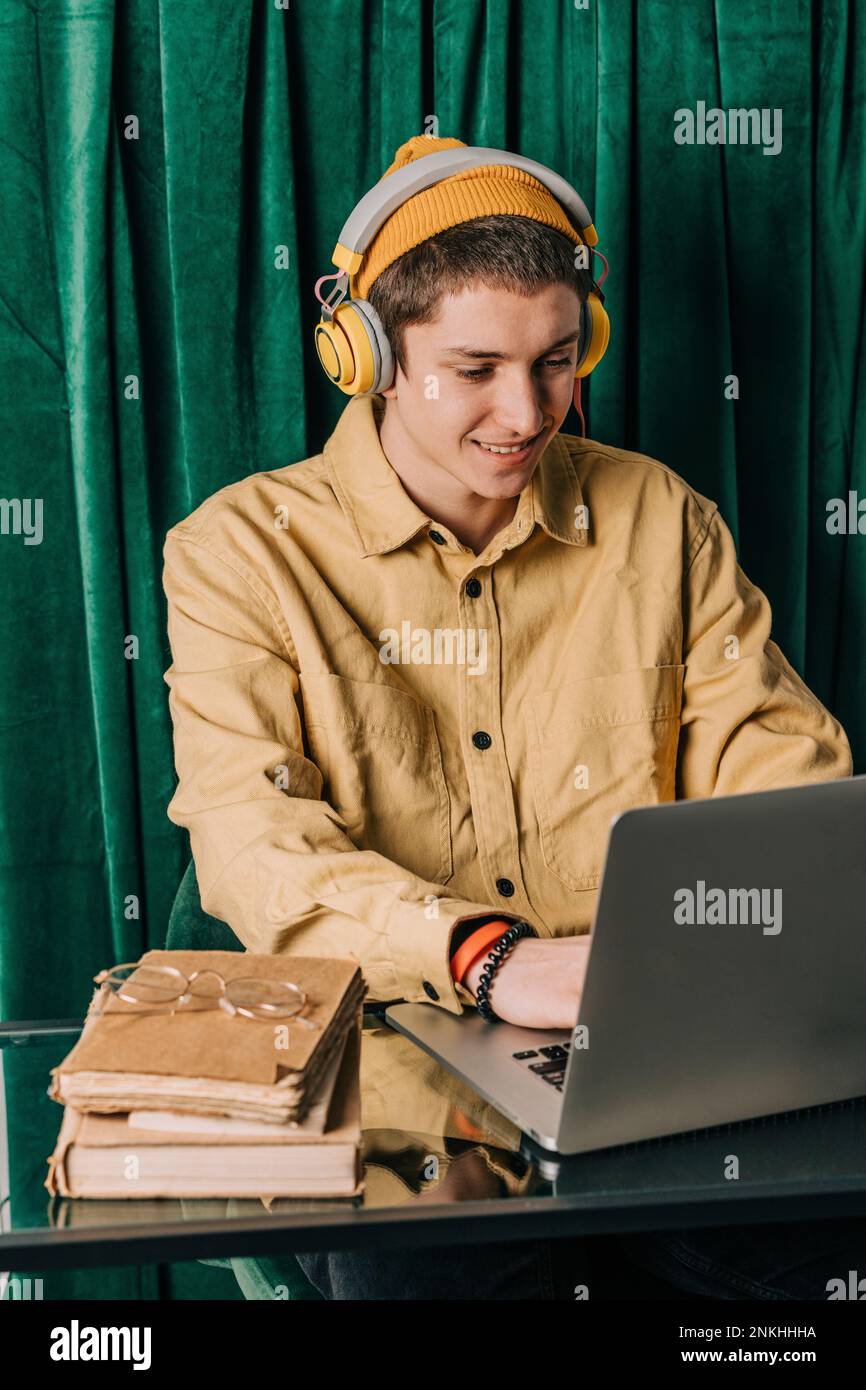 Muchacho adolescente que lleva auriculares usando el ordenador portátil en casa Foto de stock