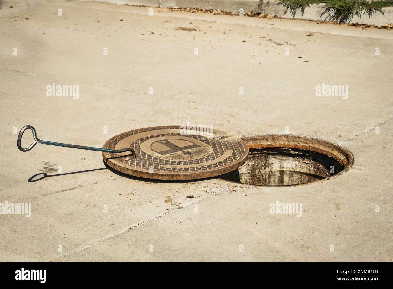 Cubierta de alcantarilla de acero pesado removida de alcantarilla en calle pavimentada con gancho todavía en cubierta - Espacio para copia Foto de stock