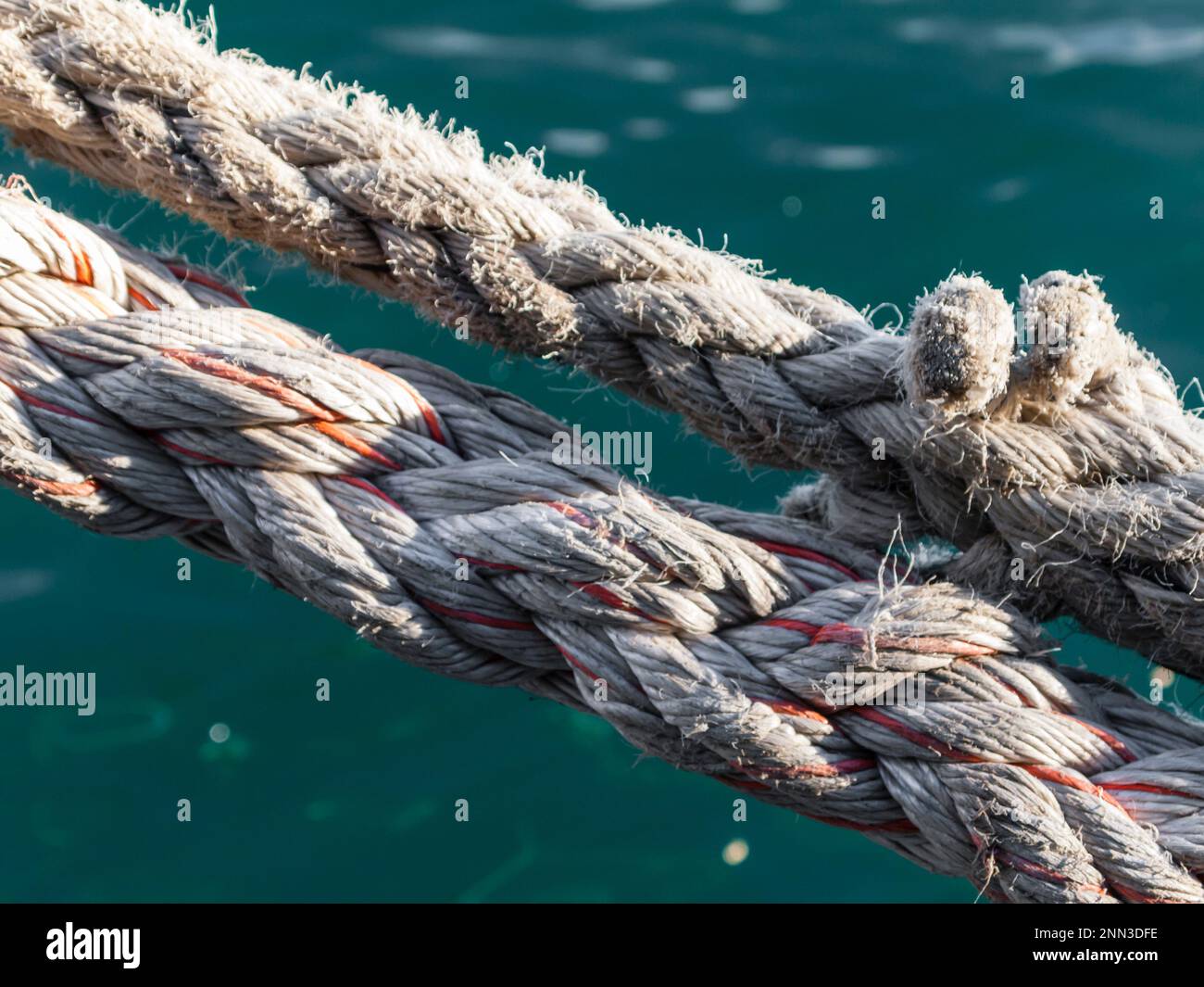 Dos cuerdas de cáñamo desgastadas para sujetar barcos en un puerto. Superficie de agua de mar Greenisch en el fondo Foto de stock