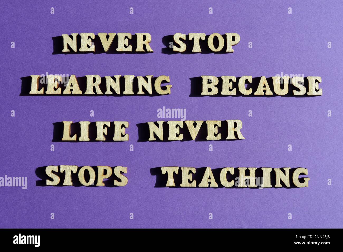 Nunca dejes de aprender porque la vida nunca deja de enseñar, frase motivadora en letras de alfabeto de madera aisladas sobre fondo púrpura Foto de stock