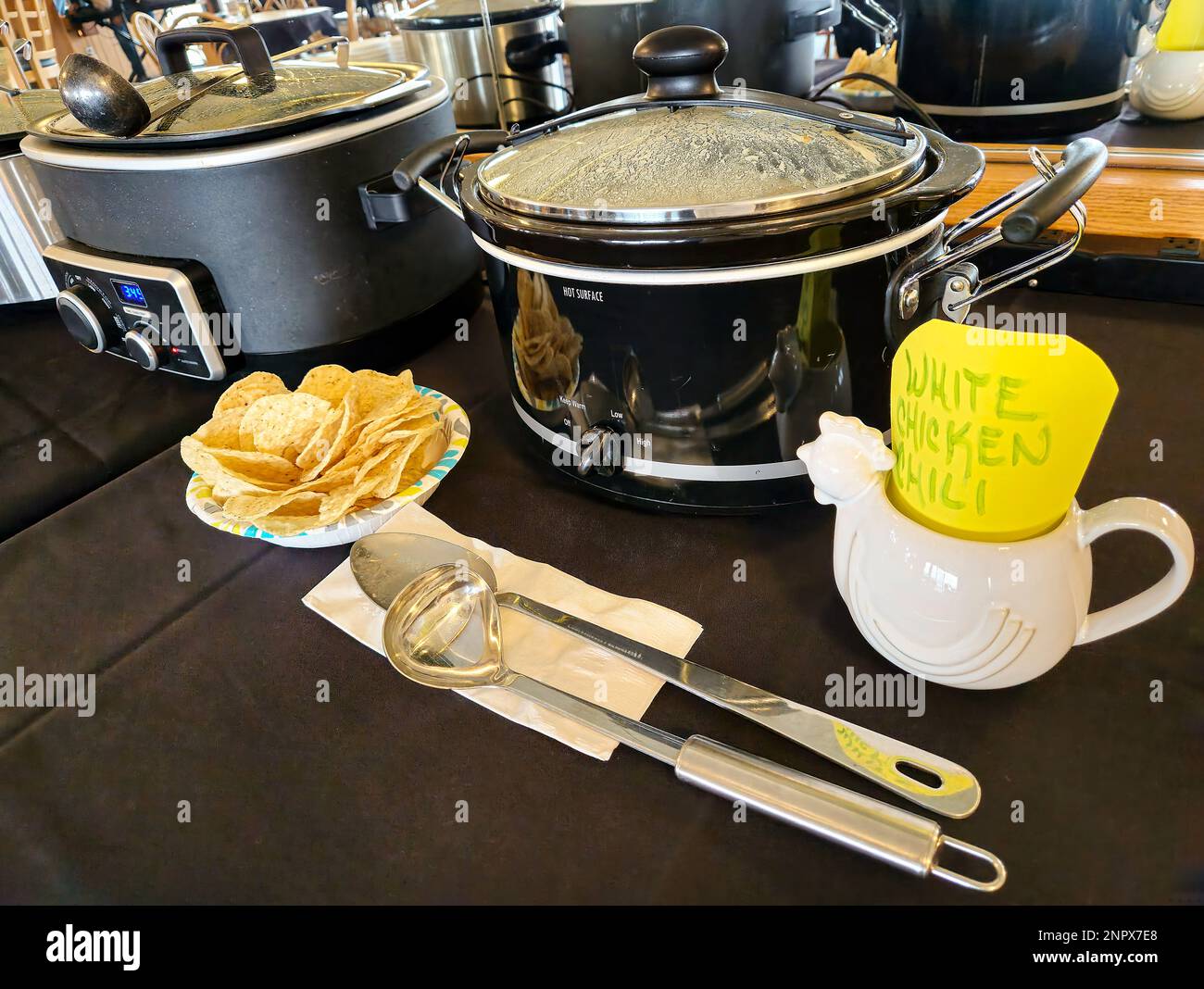 Fila de crockpots con patatas fritas y cubiertos para un concurso de cocina de chile Foto de stock